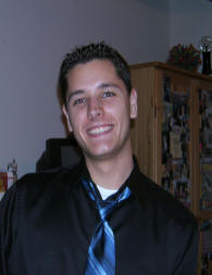 A picture of Eric Wagenhals wearing a black collared shirt and a blue and black tie.